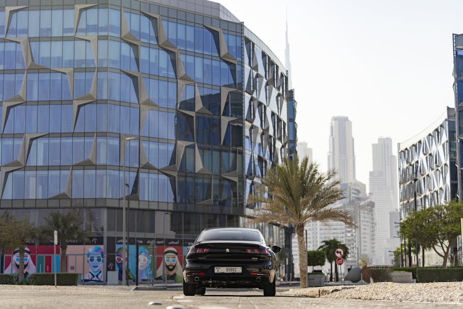 A luxury Peugeot sedan parked in the modern architectural setting of Dubai with skyscrapers in the background.